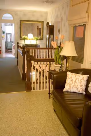 Cozy senior living interior with a couch, lamp, flowers, and a wooden staircase.