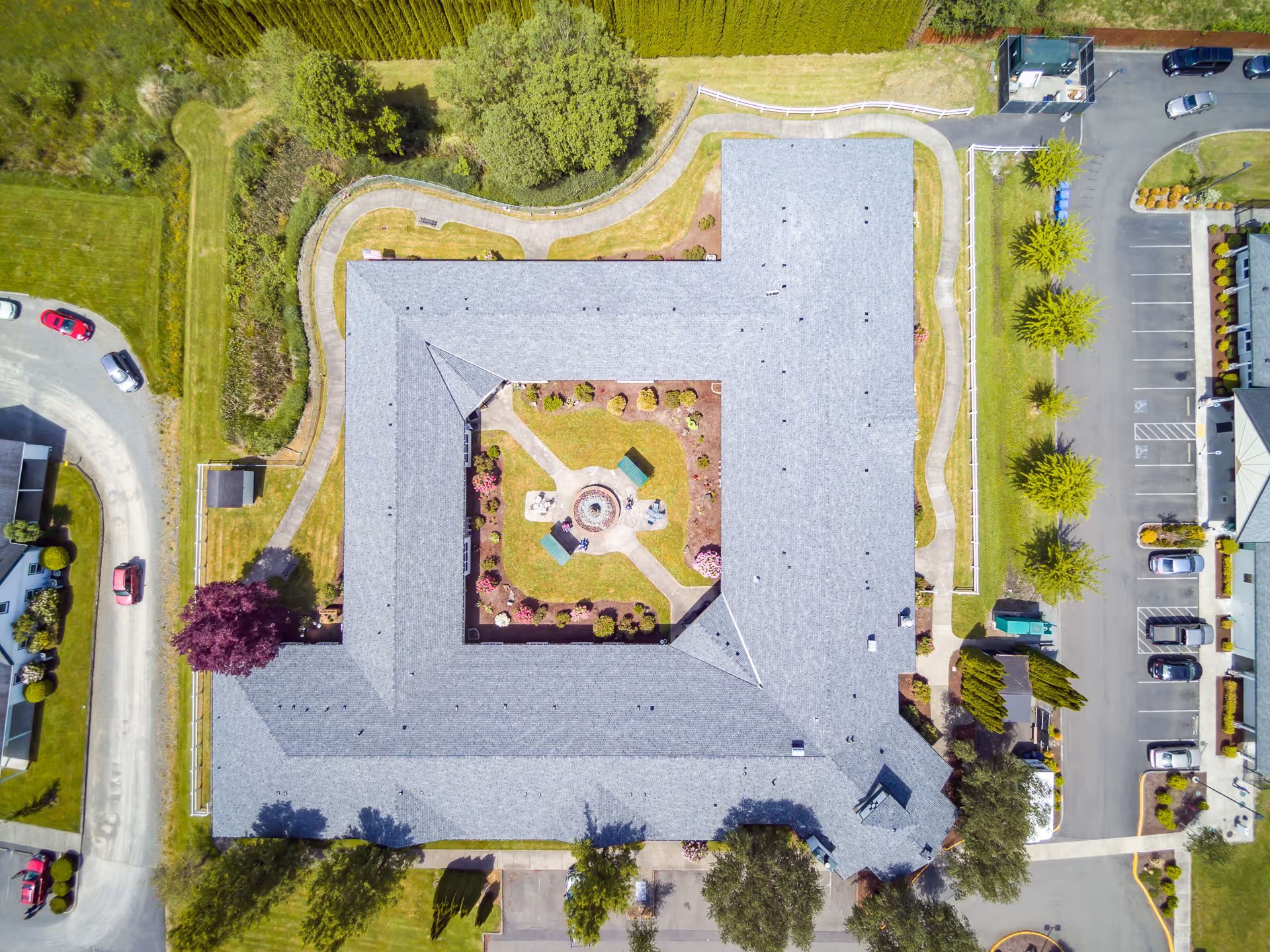 Aerial top-down view of a U-shaped assisted living building with a landscaped central courtyard, surrounding walkways and parking areas.