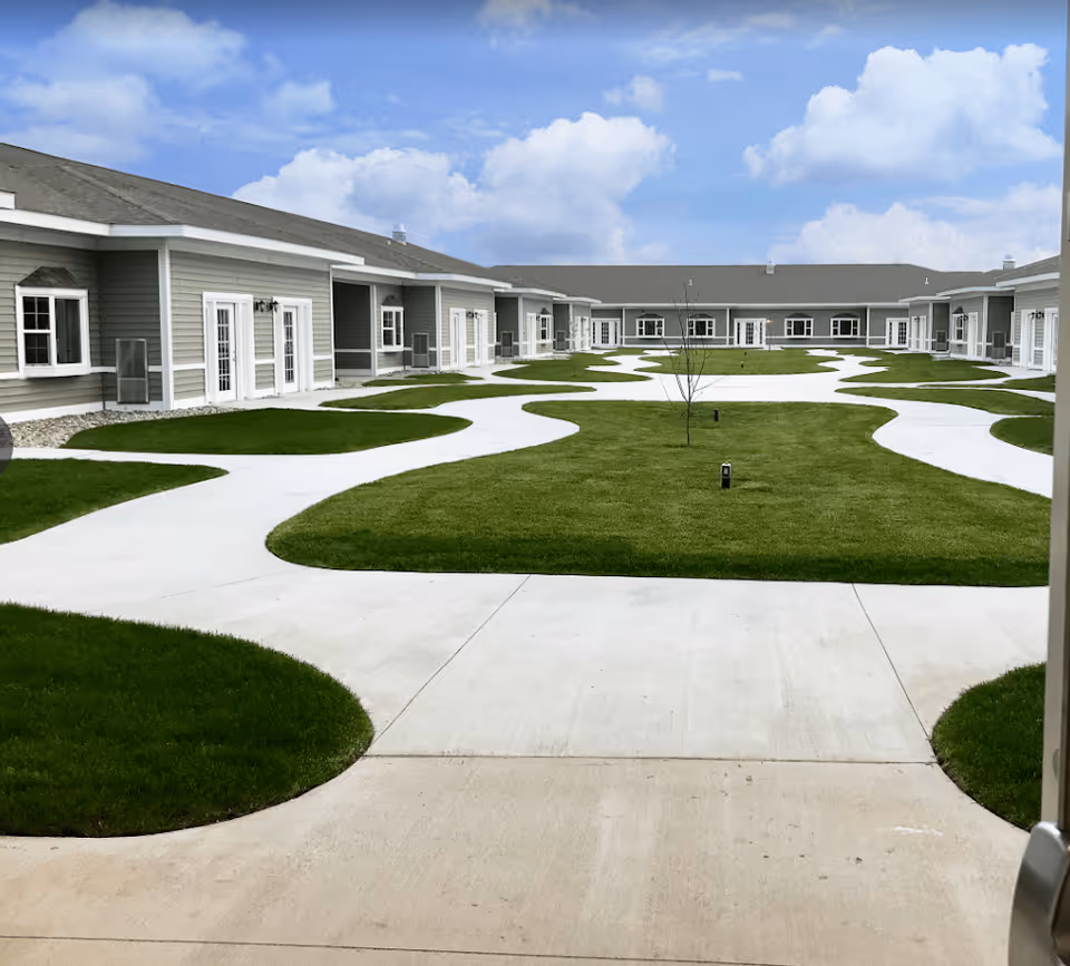 A landscaped courtyard with winding concrete pathways and single-story units surrounding a central green lawn under a blue sky.
