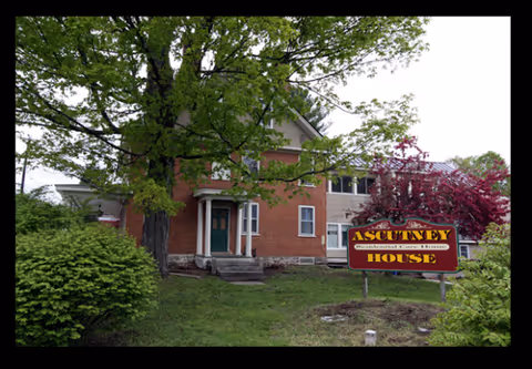 Brick senior living building with a yellow Ascutney House sign beside the lawn.