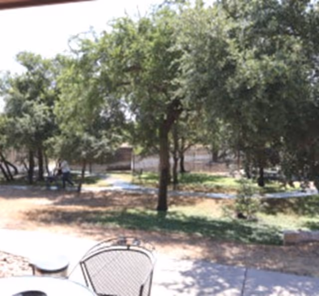 Patio with metal chairs and tables overlooking a shaded yard with trees and a walking path.