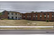 Exterior view of Towne Manor East with brick wings and a grassy front lawn.