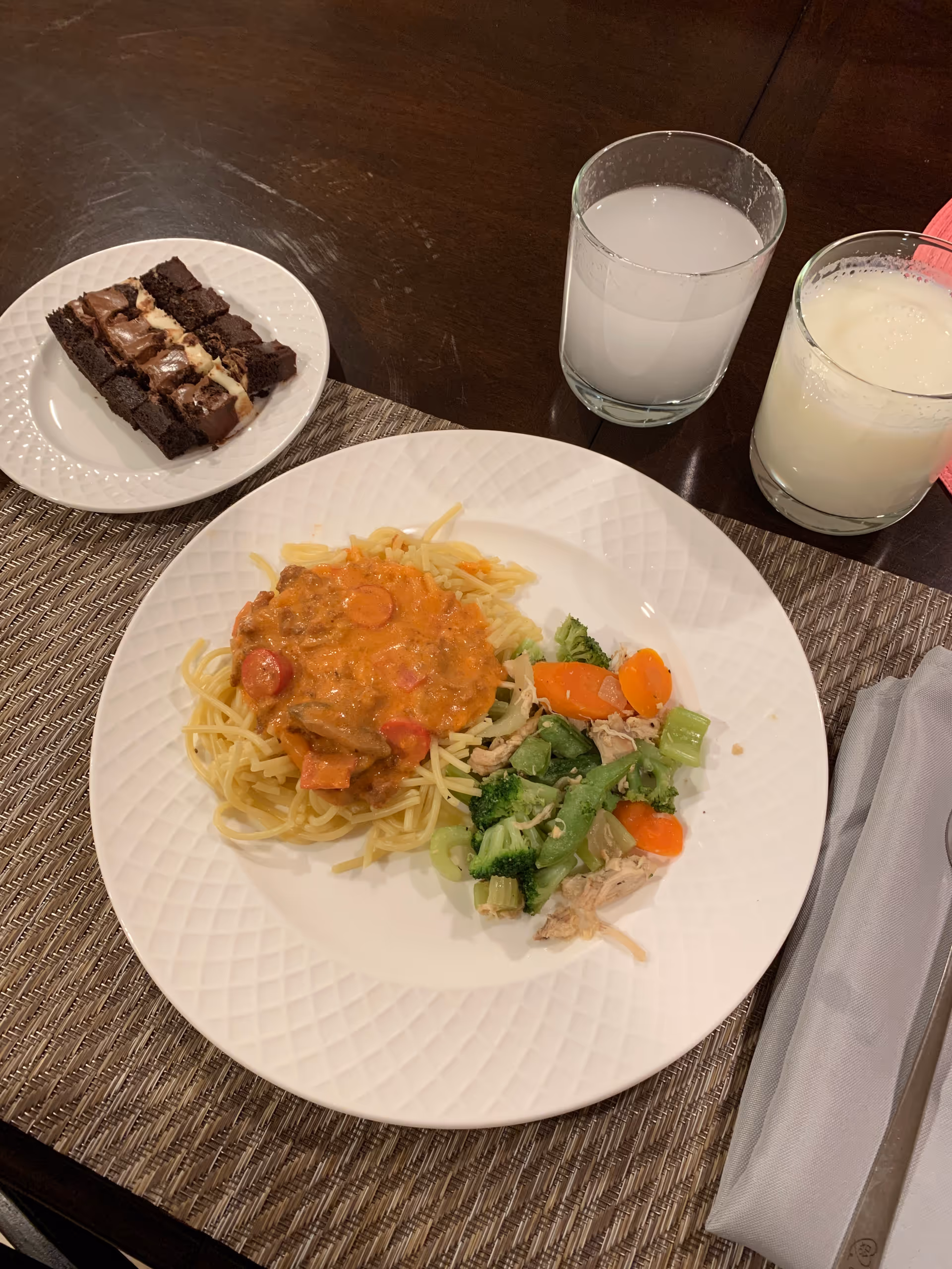 A dinner plate with spaghetti and sauce, a side of mixed vegetables, a small plate of brownies, and two drinks on a dining table.