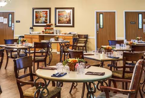 A quiet dining room with round tables, chairs, and a buffet along the back wall.