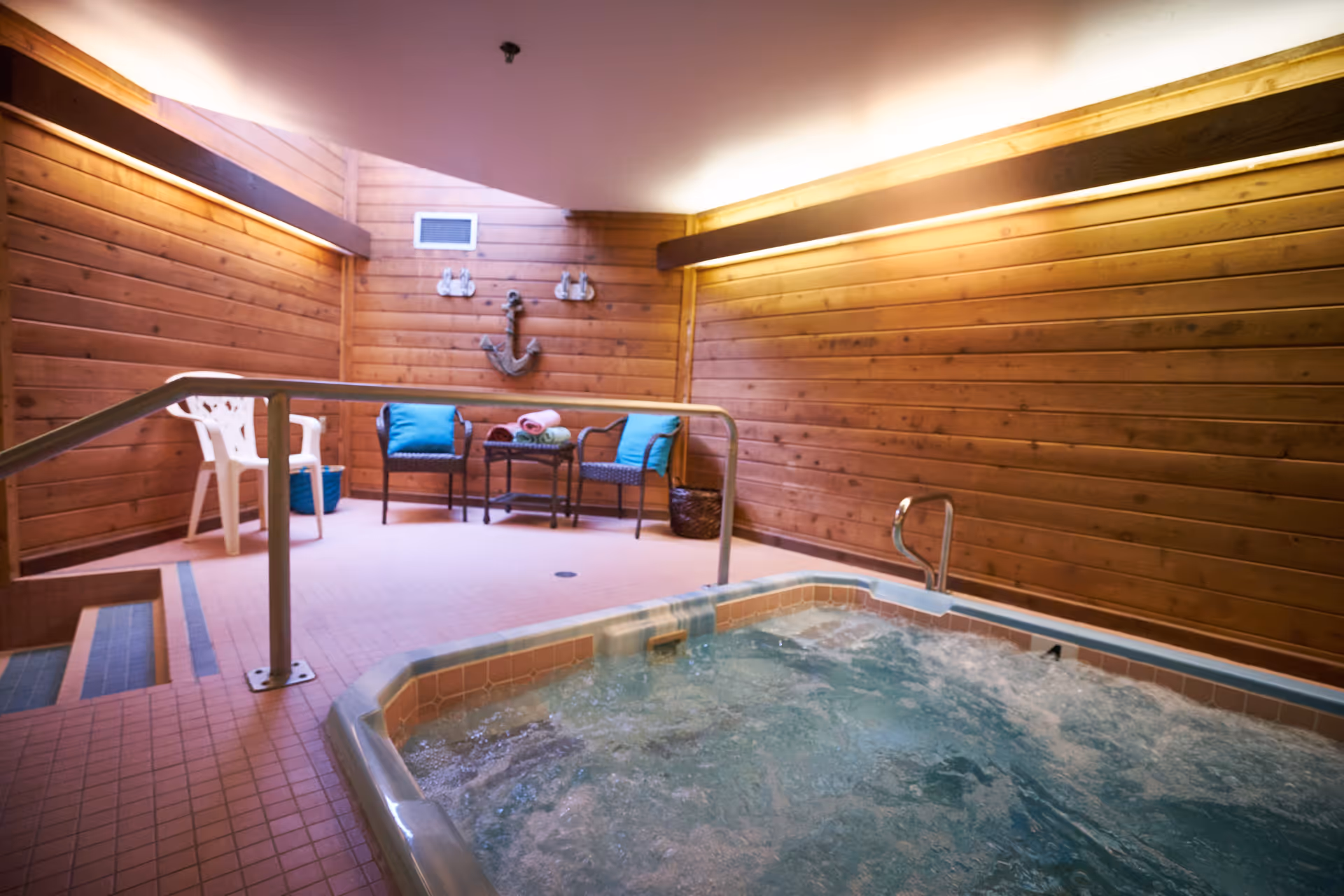 Indoor hot tub in a wood-paneled relaxation room with seating, towels, and a decorative anchor on the wall.