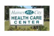 Outdoor sign for Haines City Health Care Center with green text on a white background, surrounded by grass and trees.