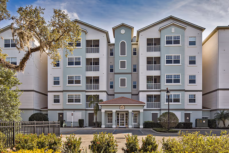 Front exterior of a four-story residential building with balconies, a central entrance, and landscaped foreground.