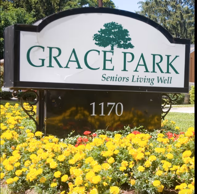 Entrance sign reading "GRACE PARK Seniors Living Well" with the address "1170" surrounded by yellow and red flowers.