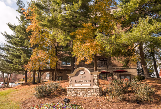 Stone sign reading "The Lafayette" in front of a multi-story brick building surrounded by trees with fall foliage.