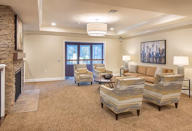 Brightly lit communal lounge with sofa, armchairs, coffee tables, a stone fireplace and windows.