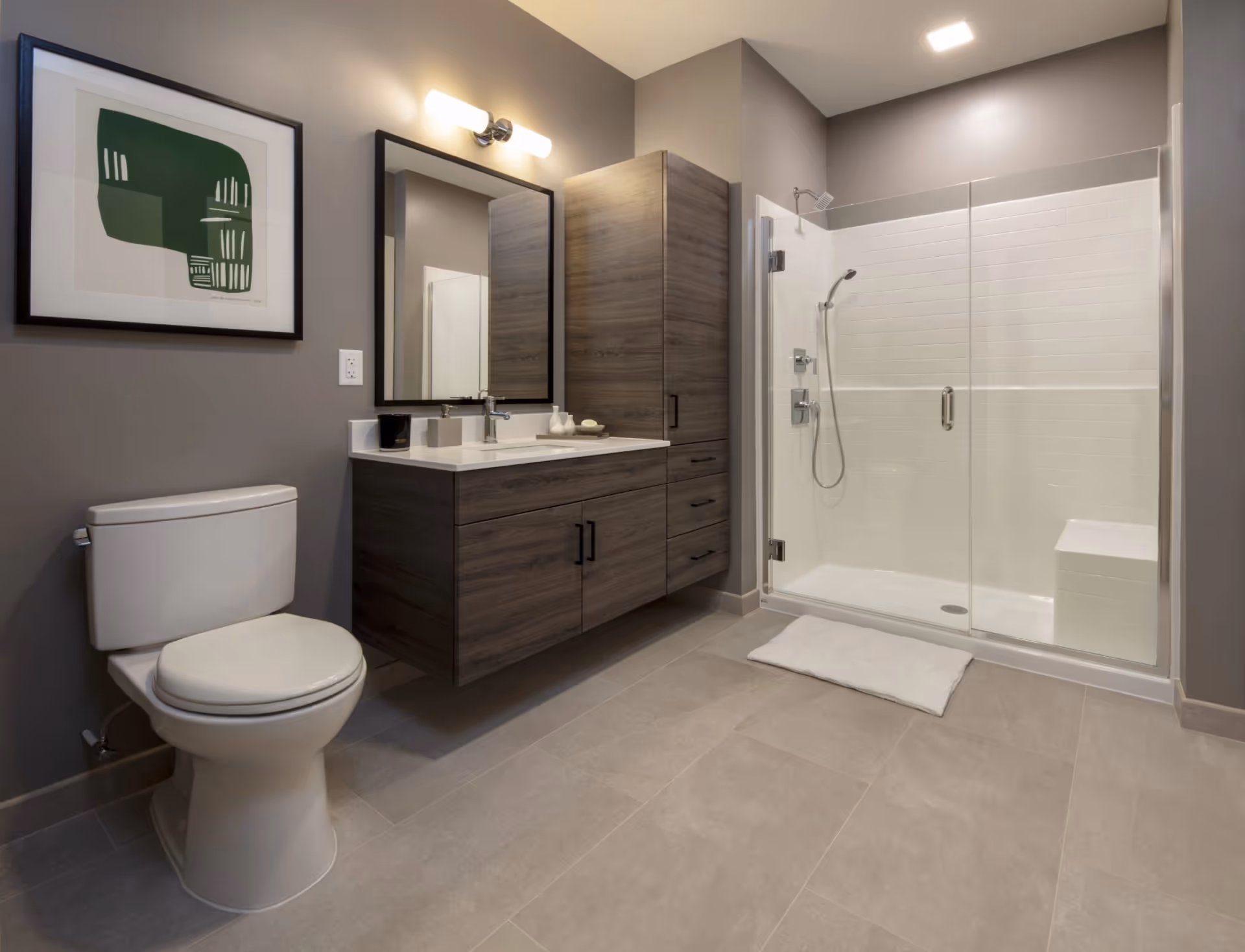 Modern bathroom with a toilet, floating wood vanity and mirror, a tall storage cabinet, and a glass-enclosed walk-in shower.
