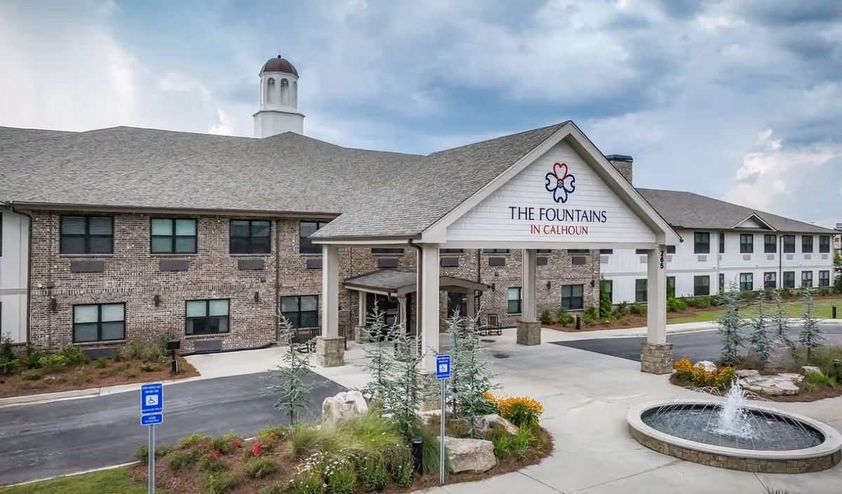 Front entrance of The Fountains in Calhoun senior living building with a porte-cochère and a circular fountain in the driveway.
