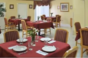 Magnolia Haven Nursing Home dining room with red tablecloths, empty tables, and soft yellow walls.