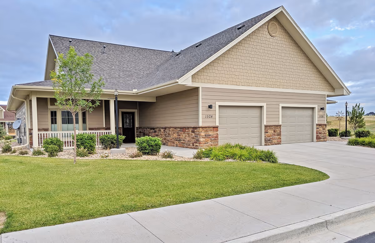 Front exterior of a single-story retirement community home with a two-car garage, covered porch, and manicured lawn.