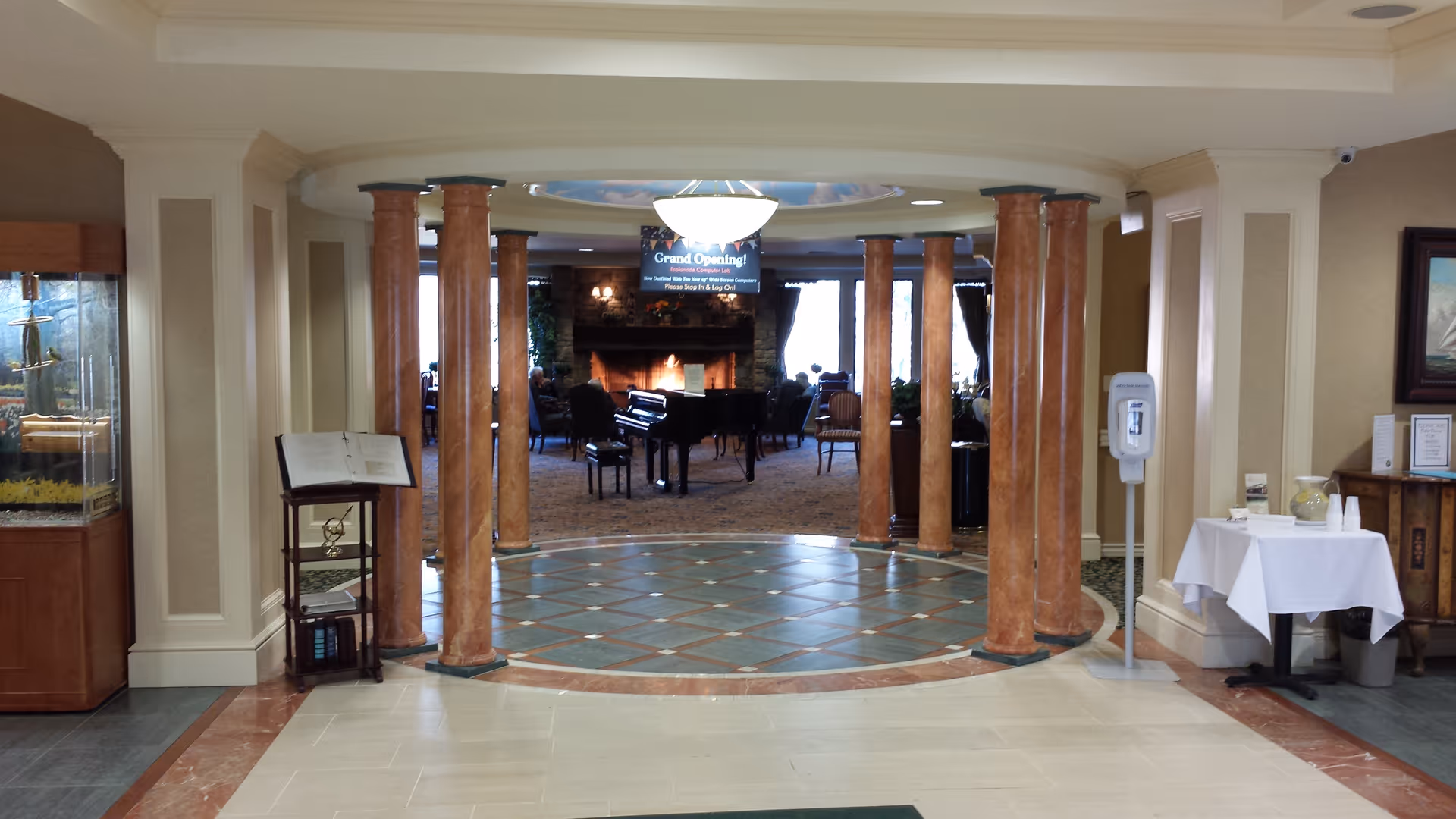 Lobby entrance with marble columns leading to a seating area featuring a grand piano and a fireplace.