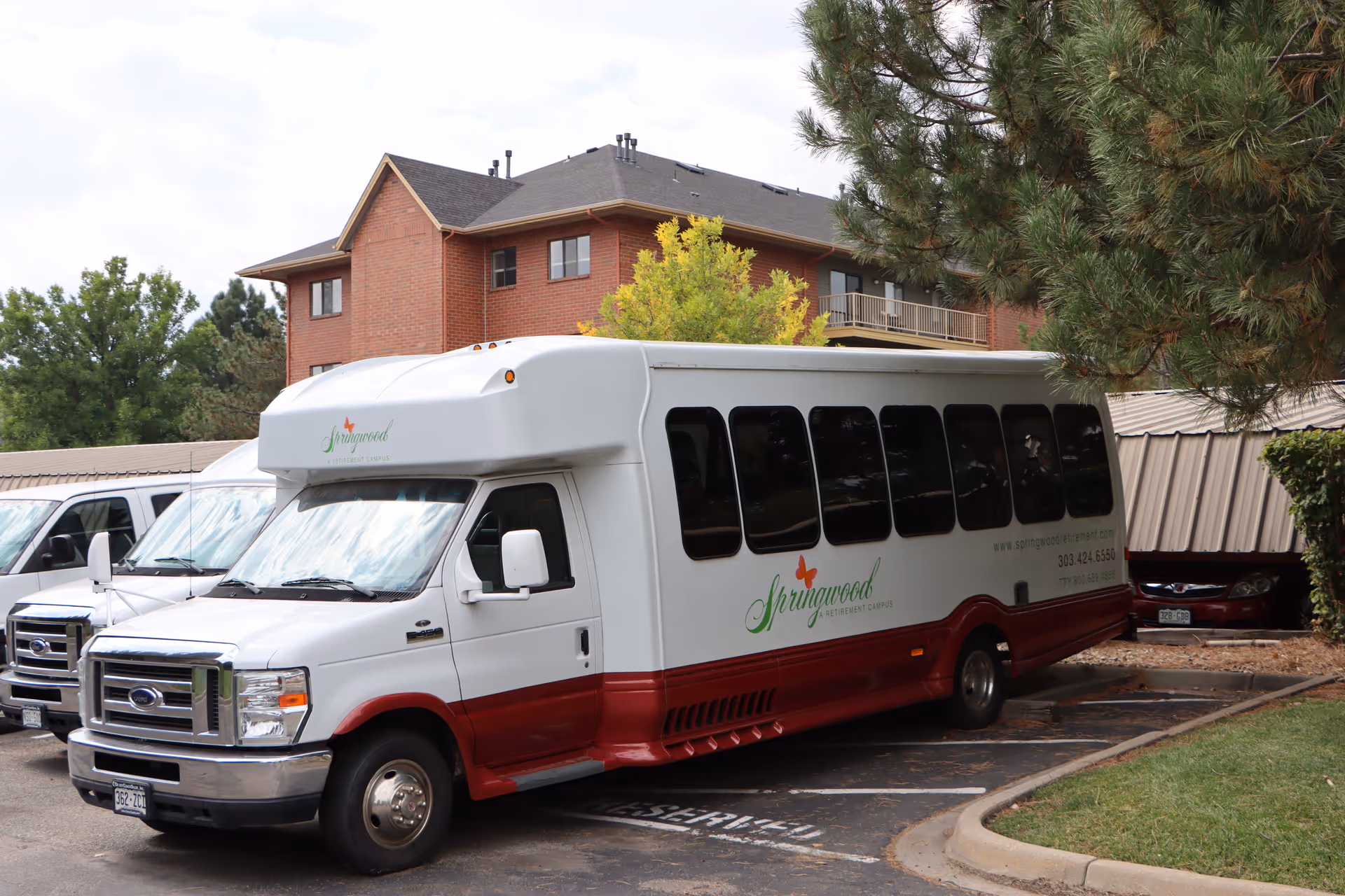 A Springwood senior living shuttle bus parked in a lot in front of a brick apartment building.