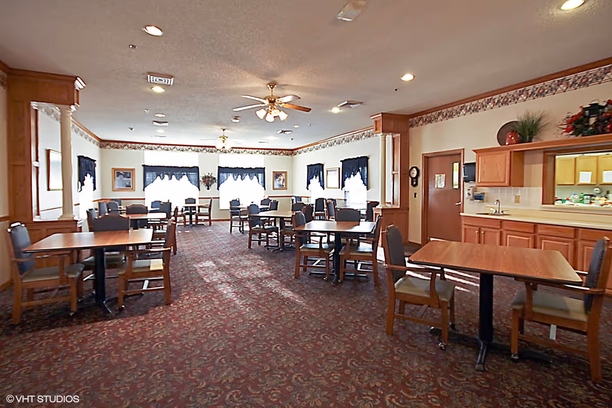 Spacious dining room with multiple tables and chairs, floral carpet, ceiling fans, and a serving counter.