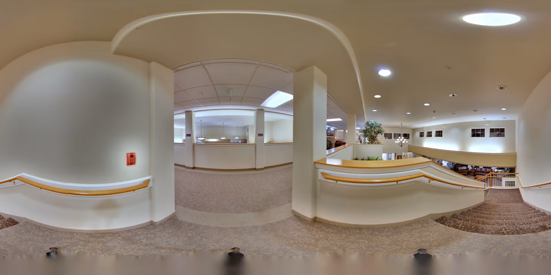 Carpeted interior stair landing and mezzanine with handrails overlooking an open lobby and seating area under recessed lighting.