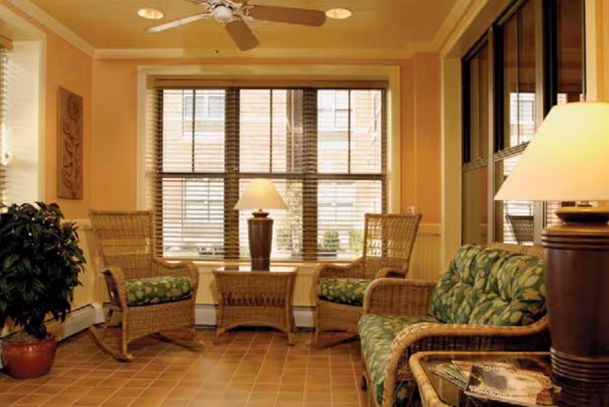 Sunlit seating area with wicker chairs, a cushioned sofa and table lamps in a cozy living room.