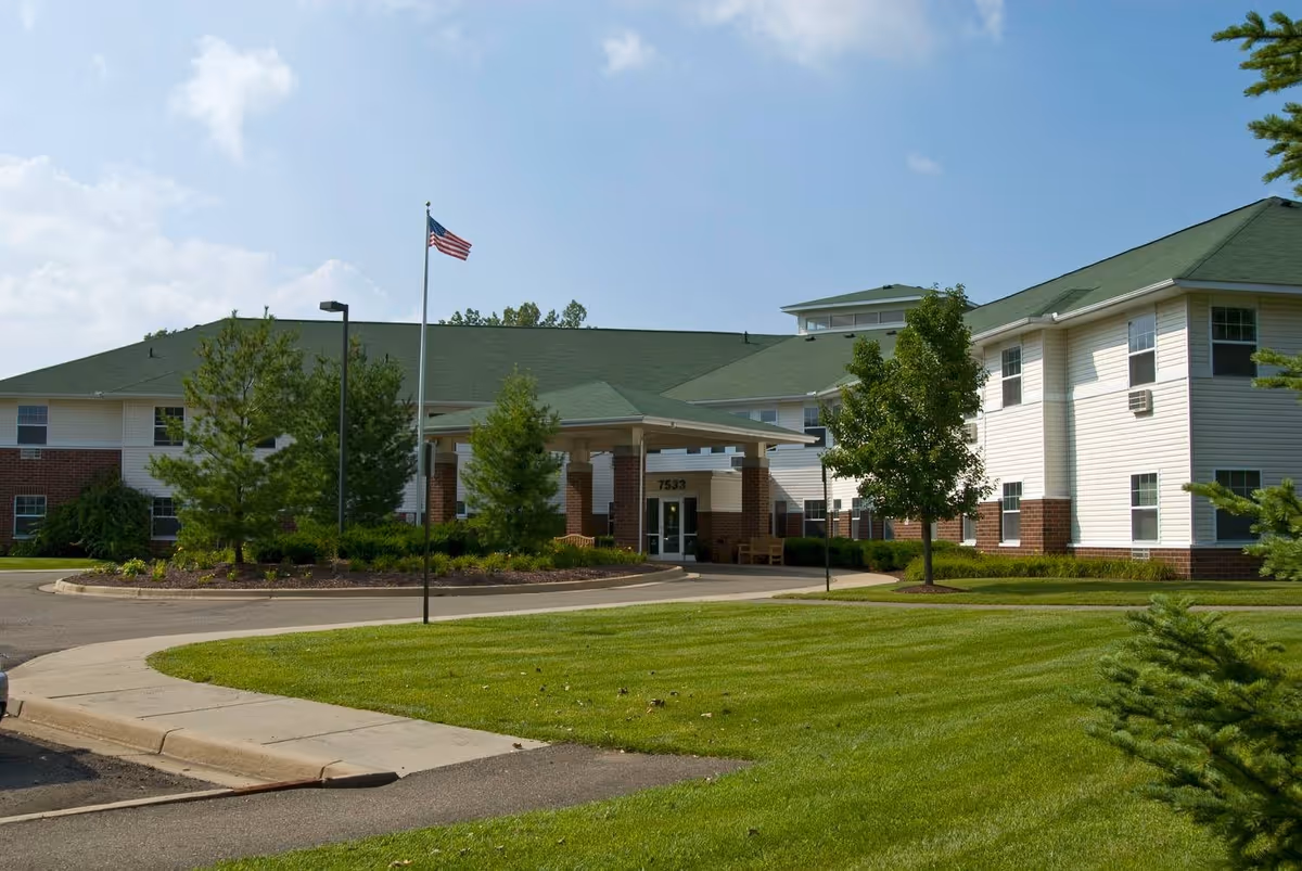 Front entrance of a multi-story senior living building with a covered driveway, American flag, and landscaped lawn.