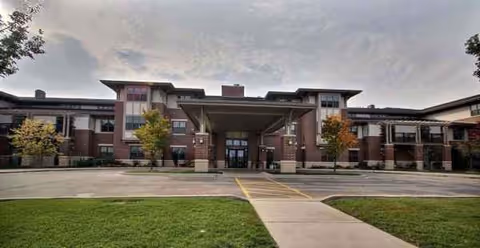 Exterior view of a senior living facility with a central entrance and surrounding lawn.