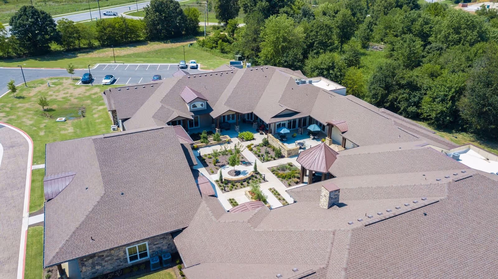 Aerial view of a senior living facility building with a central landscaped courtyard, surrounding roofs, parking area, and trees.