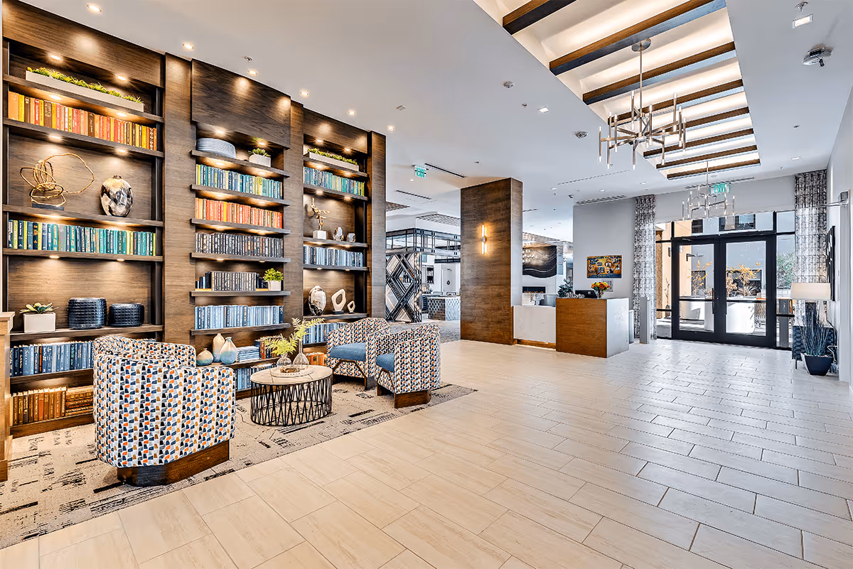 Spacious modern assisted living lobby with seating area, built-in bookshelves, and a reception desk near glass entry doors.