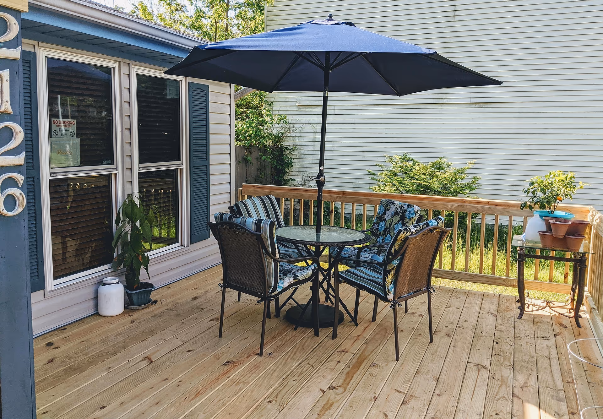 Wooden deck with a round patio table, four cushioned chairs and a large umbrella beside a house.