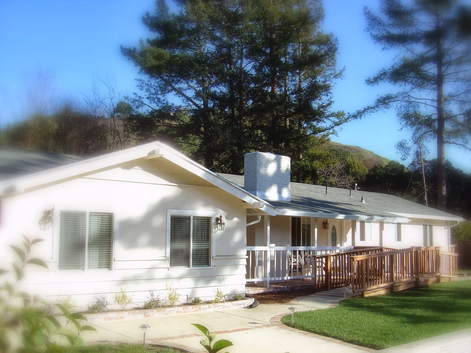 Single-story white ranch-style building with a porch and wheelchair ramp, set among trees and a green lawn.