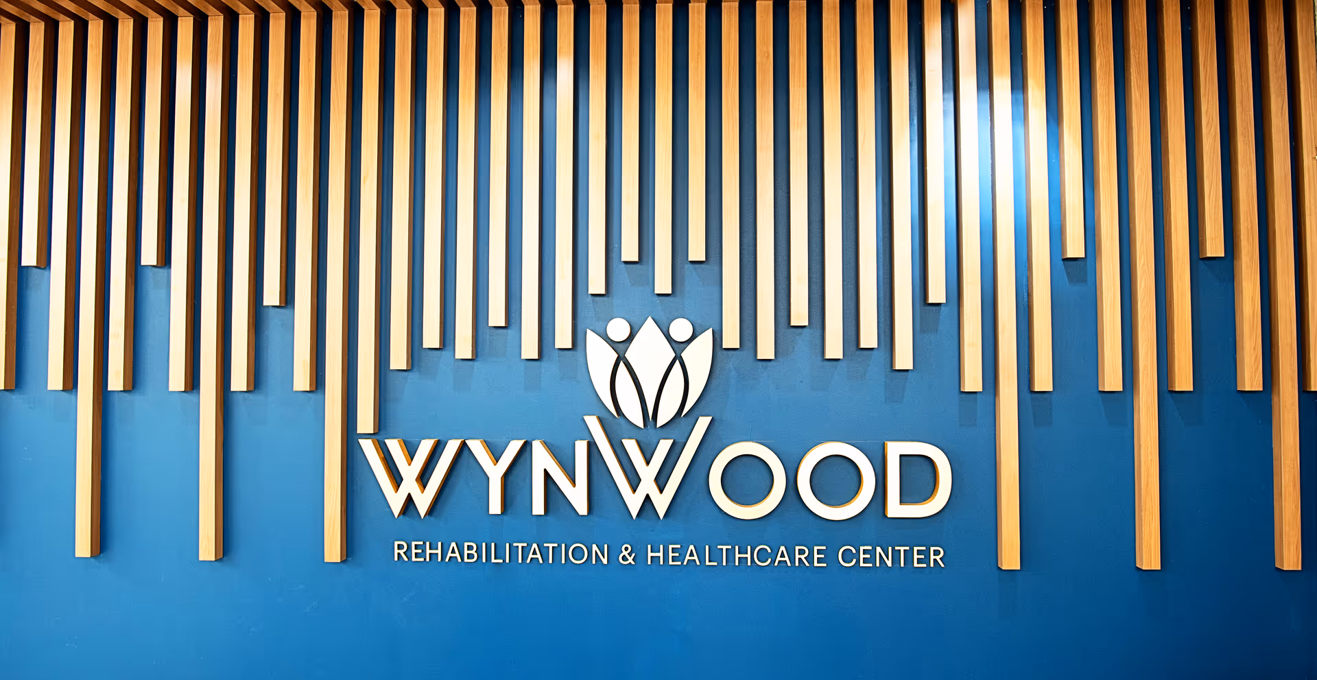 Blue interior wall with the Wynwood Rehabilitation & Healthcare Center logo and vertical wooden slats as decorative accents.