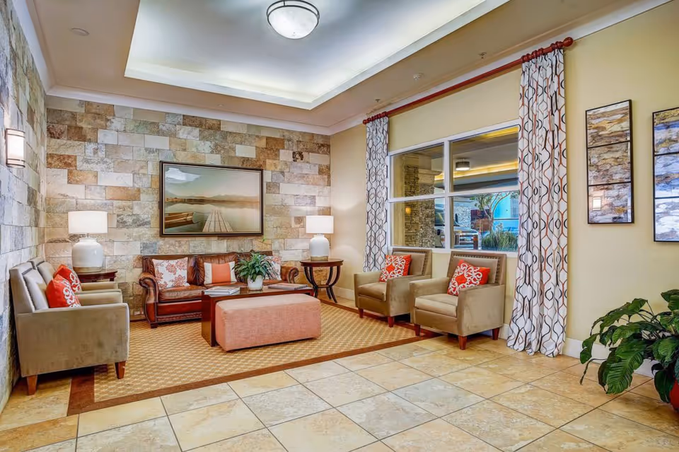 Well-lit lobby lounge with sofas, armchairs, an ottoman, lamps and a stone accent wall.