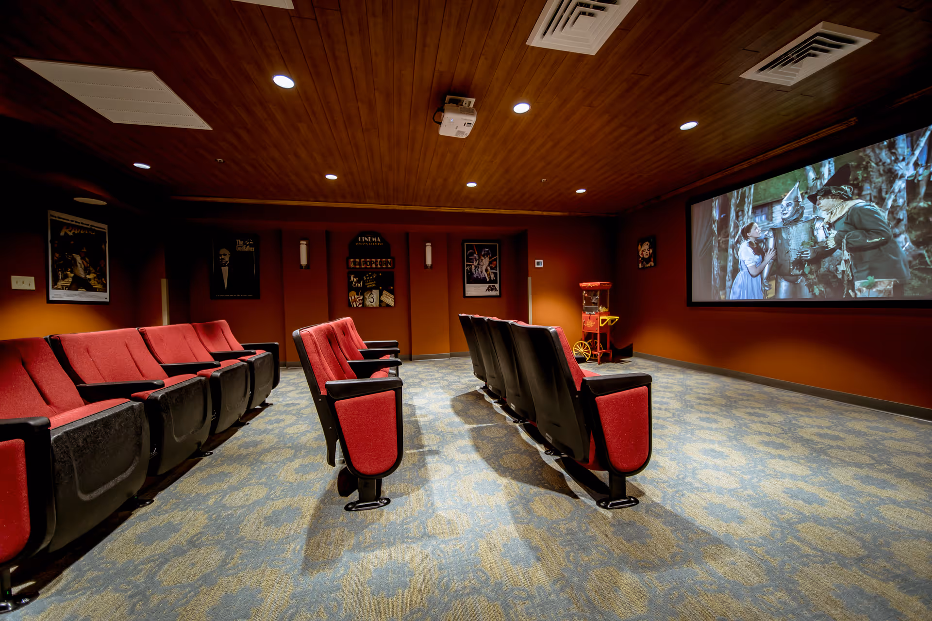 Private screening room with rows of red theater seats, a projector, a large screen showing a movie scene, and a popcorn machine.