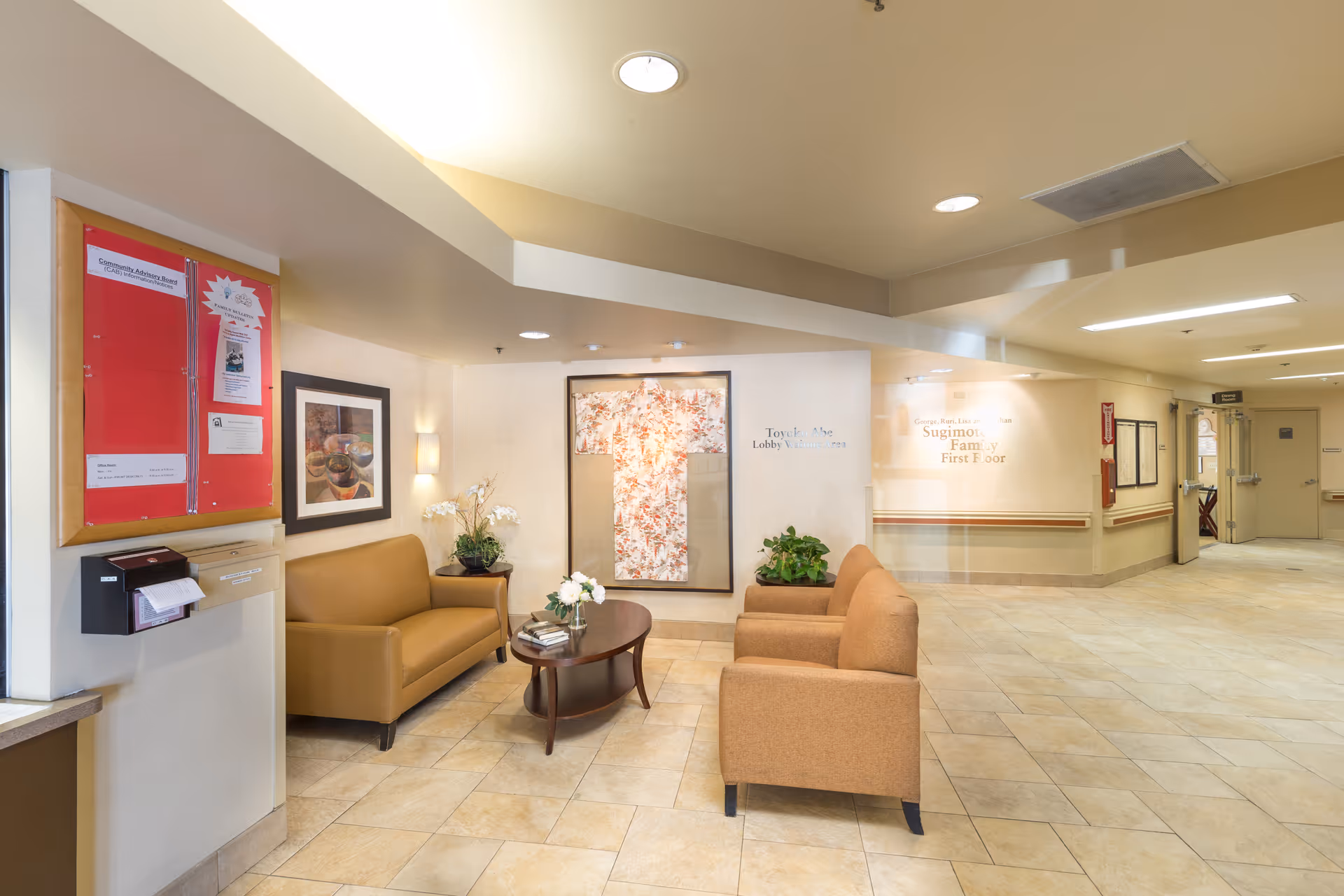 Bright healthcare facility lobby with sofas, armchairs, a coffee table, plants, and wall artwork.
