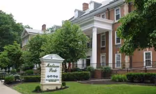 Brick building with white columns, trees, and a Madison Park sign.