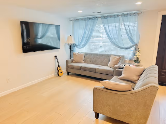 Cozy living room in Peaceful Living Care Home with couch, TV, guitar, and bright windows.
