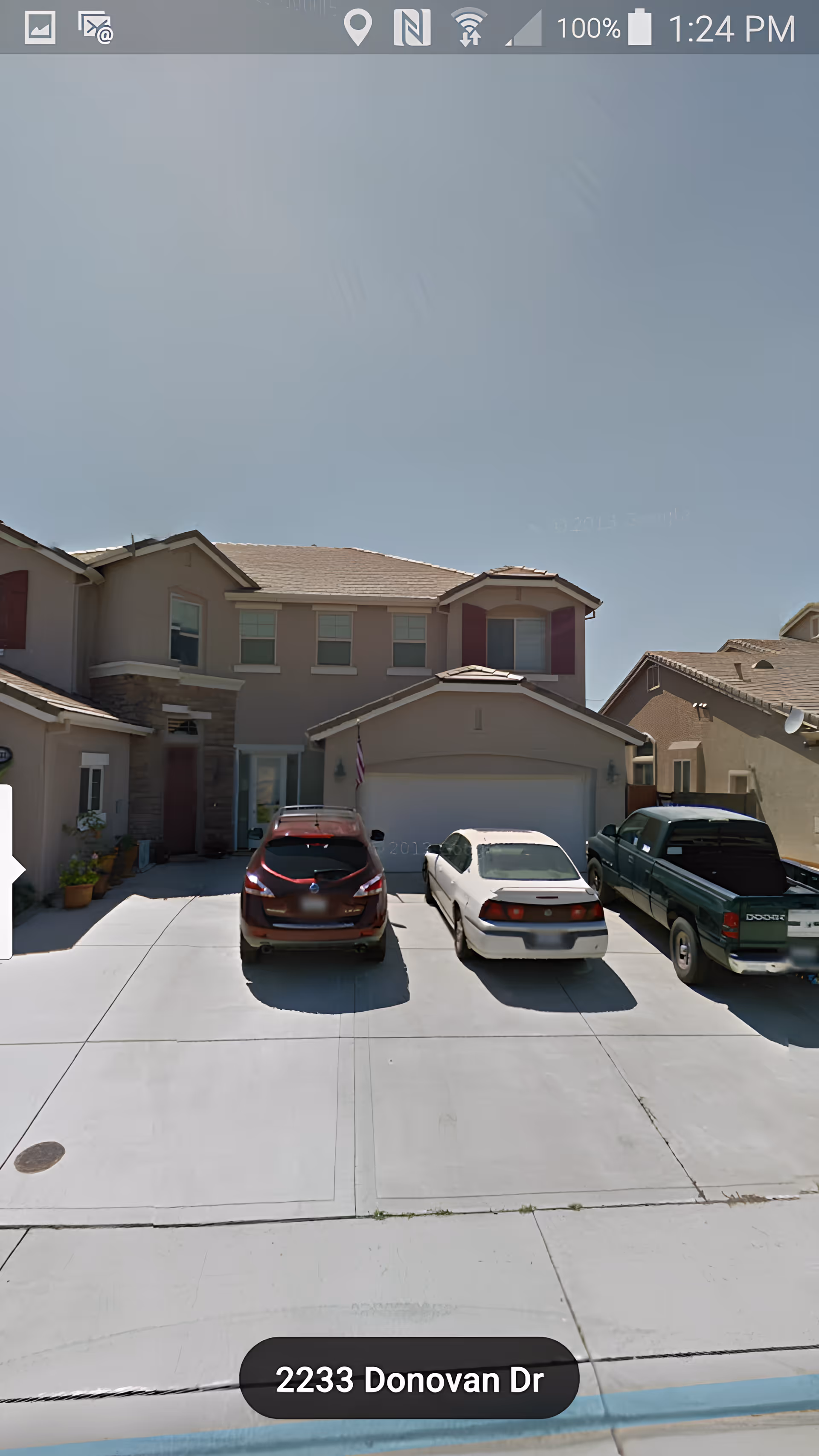 Front exterior view of a two-story residential house with a driveway containing three parked vehicles: a red SUV, a white sedan, and a green pickup truck. The house has beige walls, a tiled roof, and several windows with shutters. The address 2233 Donovan Dr is visible at the bottom of the image.