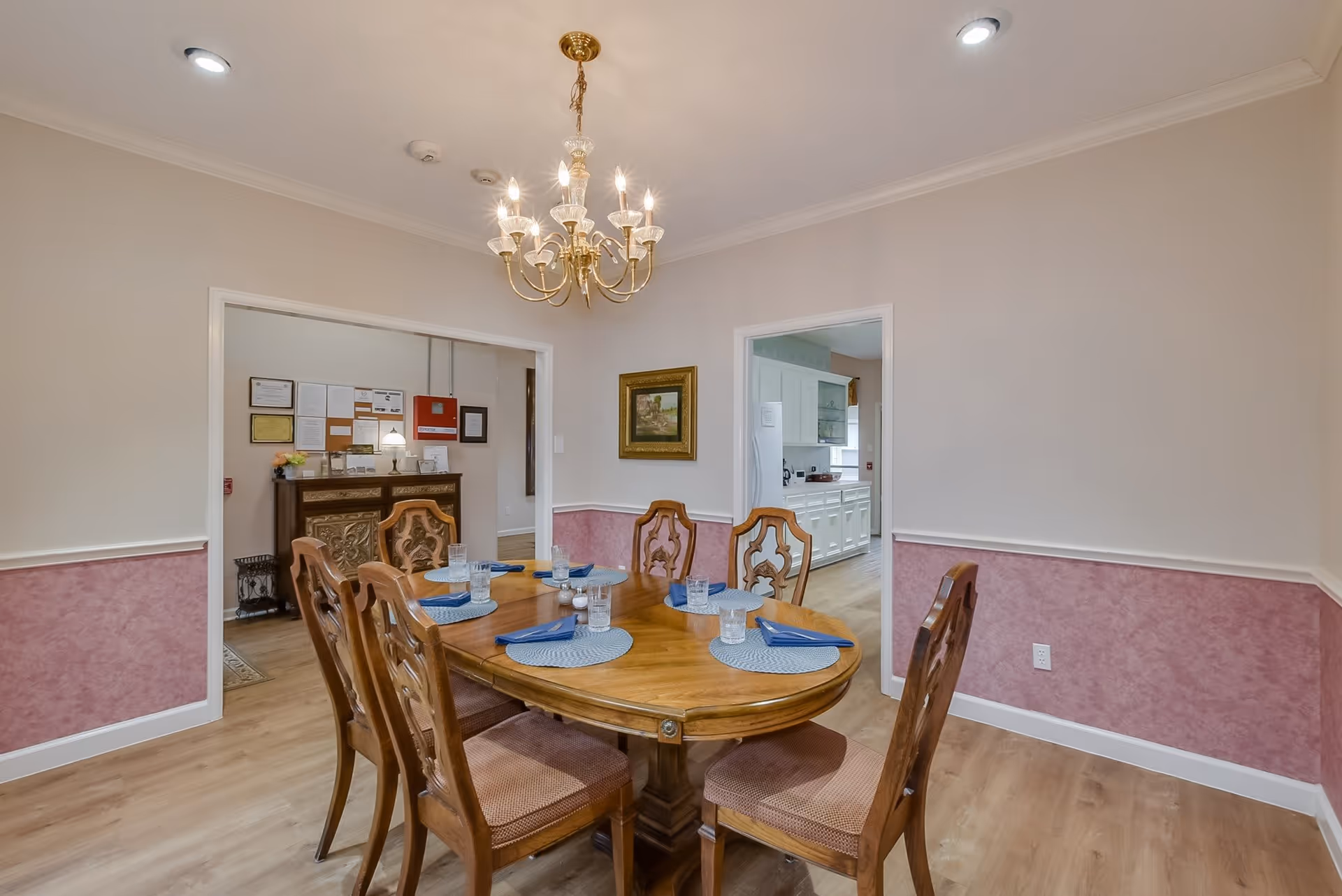 Dining room with a wooden table set for six under a chandelier and doorways leading to adjacent rooms.