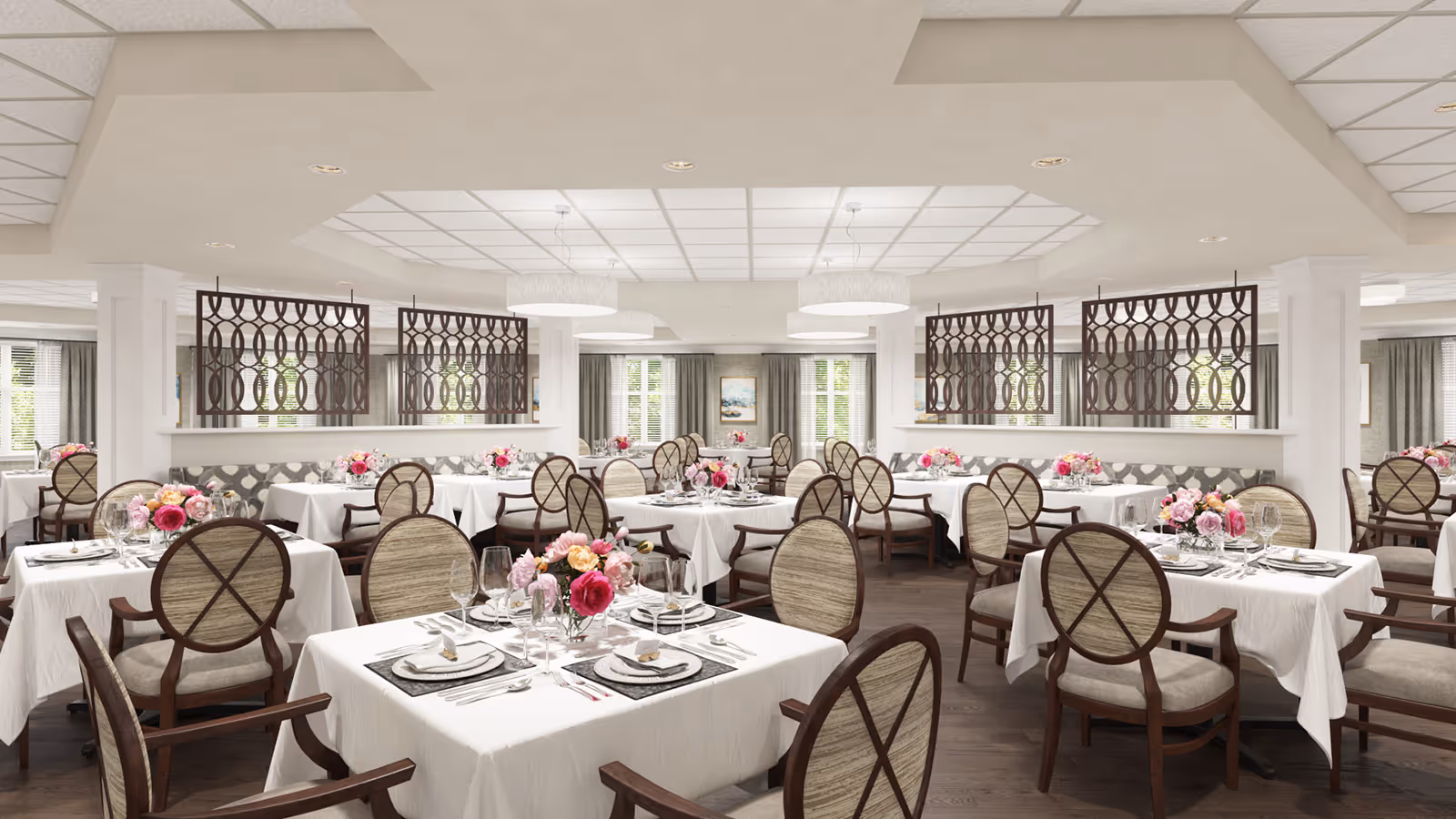 Elegant dining room with white-tablecloth tables, floral centerpieces, and round-backed wooden chairs under recessed lighting.
