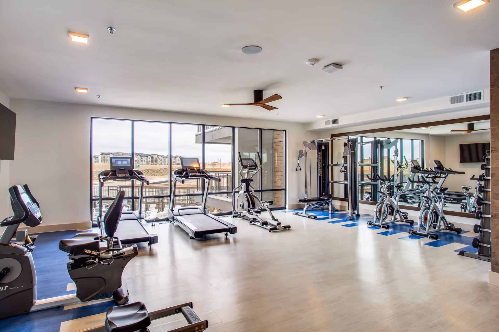 Well-lit fitness room featuring treadmills, stationary bikes, weight machines and large windows with a view.