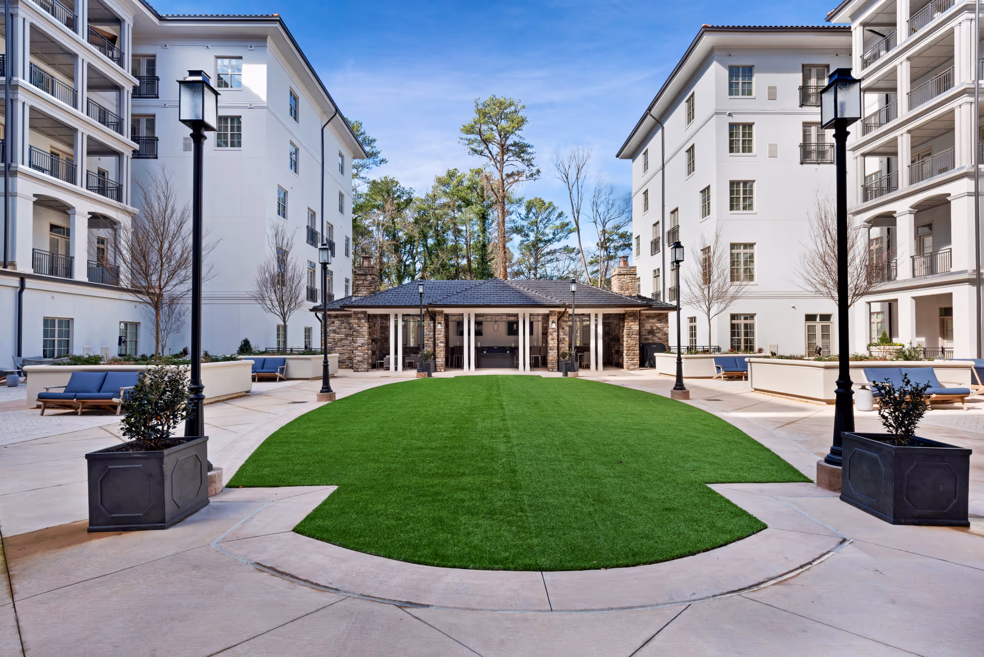 A landscaped central courtyard with a green lawn, benches, lampposts and surrounding multi-story white residential buildings.