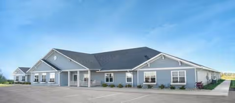 Single-story blue-gray senior living facility with a wide front entrance and parking lot.