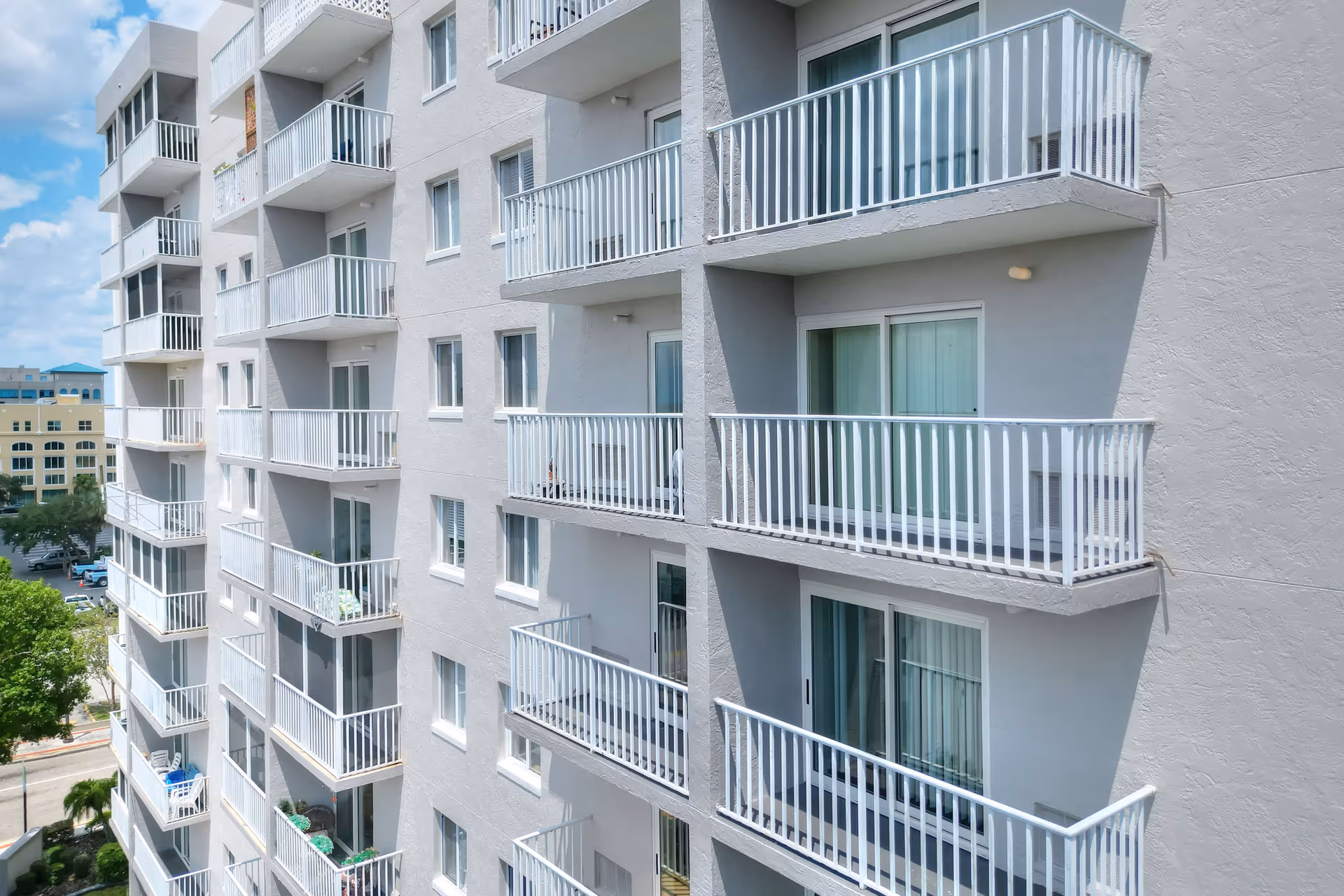 Exterior view of a multi-story residential building with rows of white balconies and sliding glass doors.