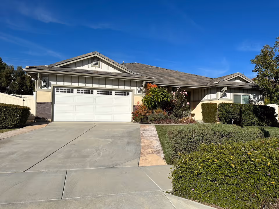 Single-story house with a two-car garage, driveway, and landscaped front yard under a clear blue sky.