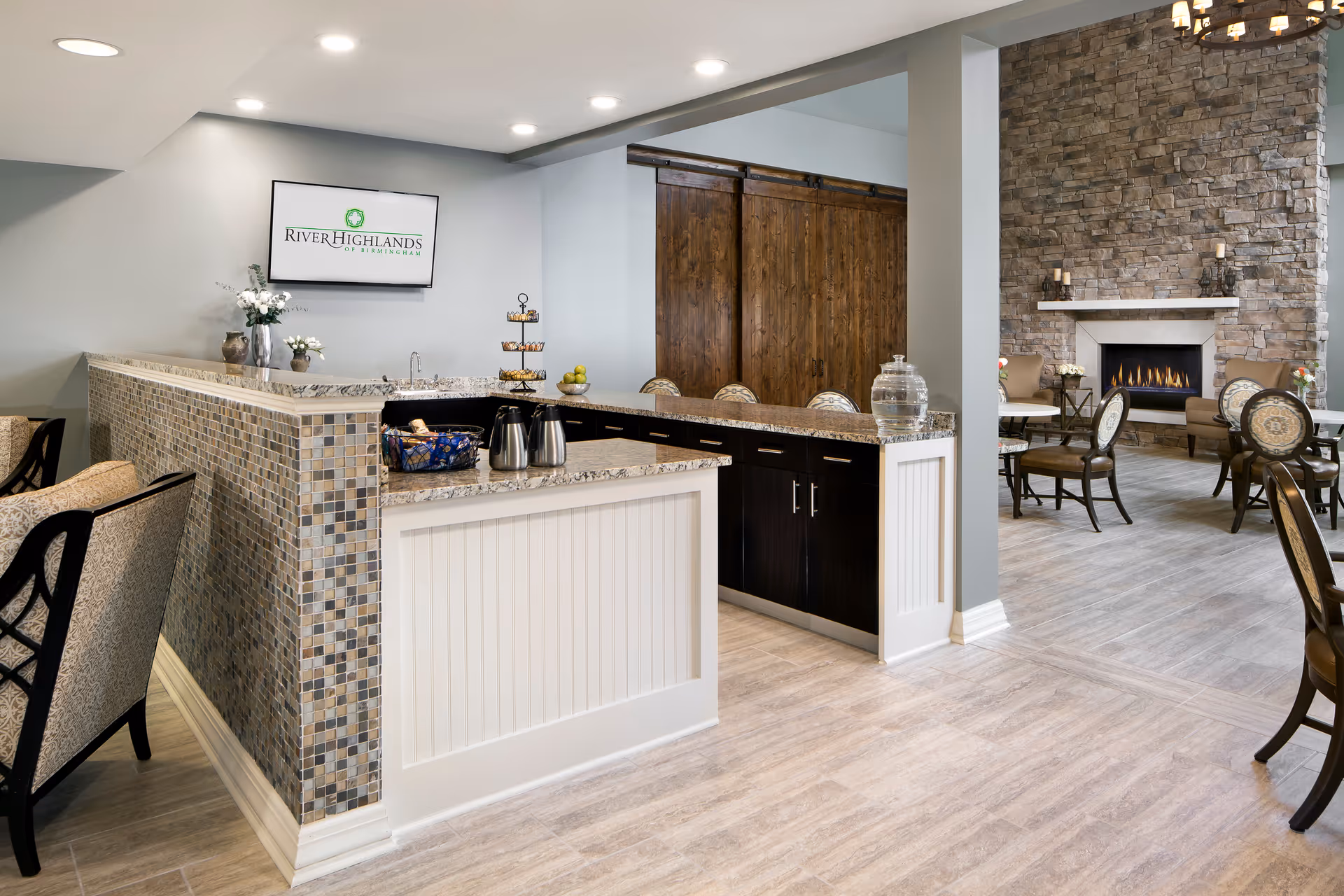 A bright communal lounge and dining area with a service counter, seating, and a stone fireplace.
