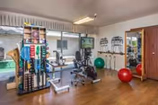 An interior fitness room with exercise machines, weights, balls, and a window view.