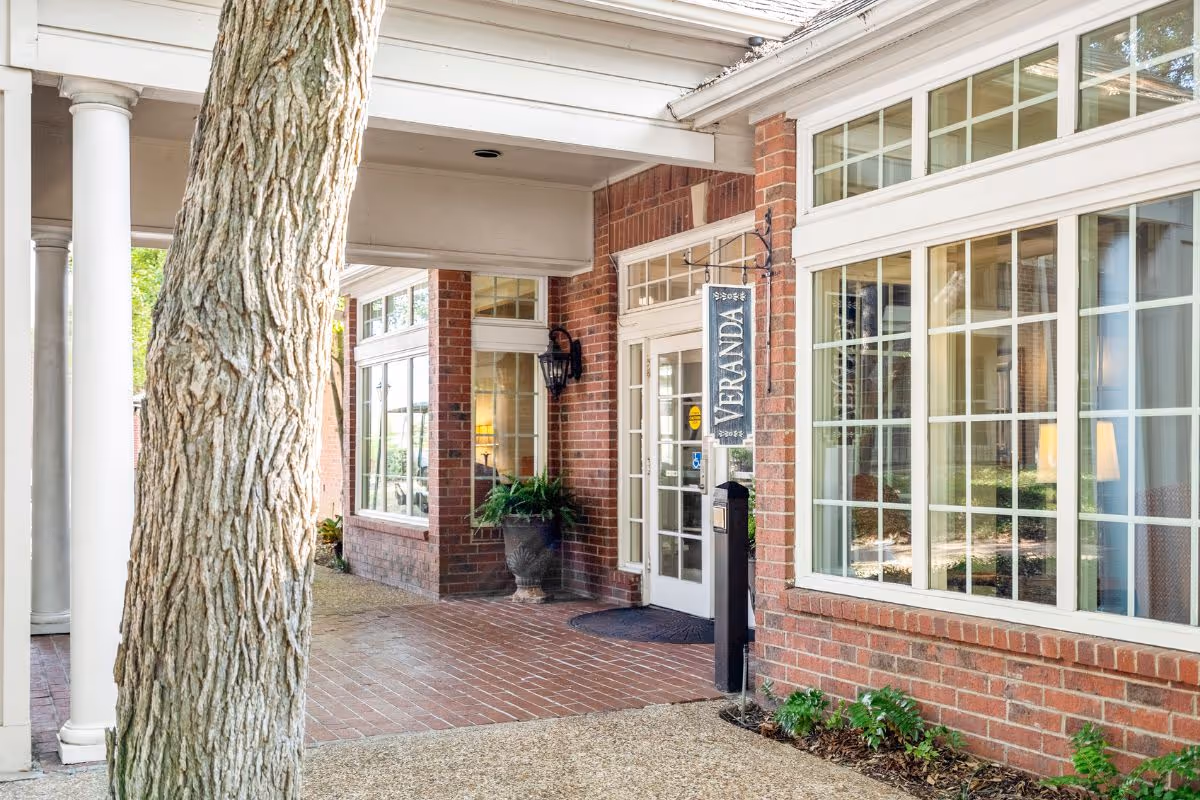 Covered brick entryway with large mullioned windows, columns, and a hanging 'VERANDA' sign.