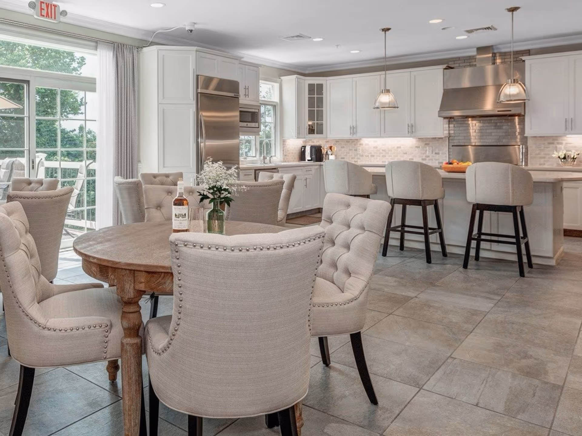 Bright open kitchen and dining area with tufted upholstered chairs around a round wooden table and a white kitchen island with barstools.