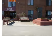 Brick building entrance with a maroon awning reading "Riverside Rest Home Main Entrance", benches and a raised circular planter on a paved forecourt.