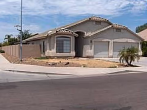 Single-story stucco house with a tiled roof and two-car garage on a corner lot with a dry front yard.