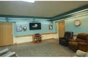 Community lounge with teal walls, a wall-mounted TV, reclining chairs, and a clock on the wall.